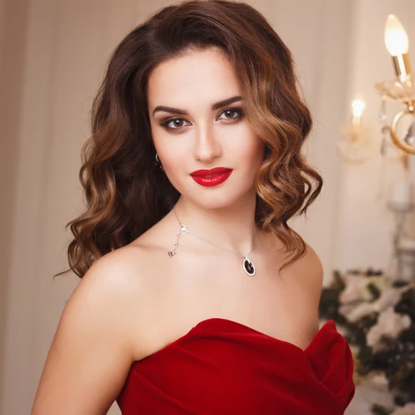 Beautiful young woman with perfect make up and hair style in gorgeous red evening dress in expensive luxury interior