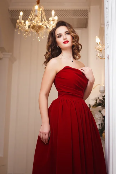 Beautiful young woman with perfect make up and hair style in gorgeous red evening dress in expensive luxury interior