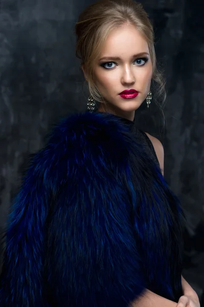 Close-up portrait of gorgeous blonde young woman in celebrity style with perfect make up and hair style wearing blue fur. Fashion beauty photo, dramatic look