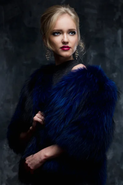 Close-up portrait of gorgeous blonde young woman in celebrity style with perfect make up and hair style wearing blue fur. Fashion beauty photo, dramatic look