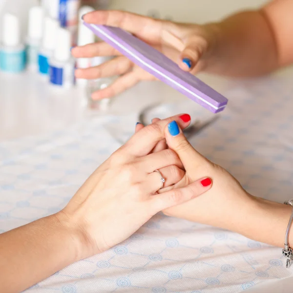 Closeup shot of a woman in a nail salon receiving a manicure by a beautician with nail file. Woman getting nail manicure. Beautician file nails to a customer.