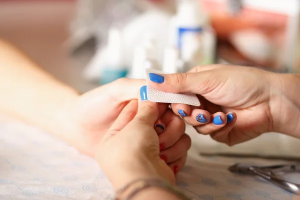 Closeup shot of a woman in a nail salon receiving a manicure by a beautician with nail file. Woman getting nail manicure. Beautician file nails to a customer.