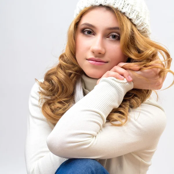 Close-up portrait of a blonde girl in a warm white pullover and hat isolated on white background