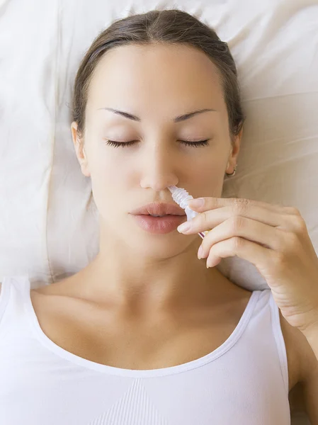 Sick young woman using ayurvedic nasal spray and laying on sofa