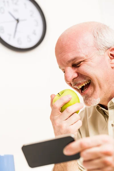 Happy senior man eating and using phone at work