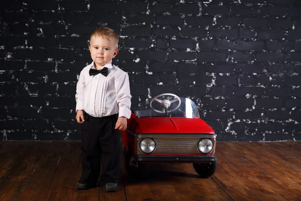 Little boy plays with red toy car, black background