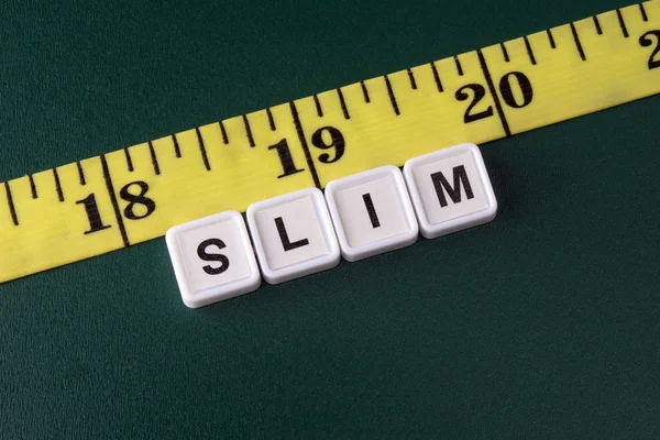 Arrangement of alphabet blocks of word SLIM with yellow tape measure