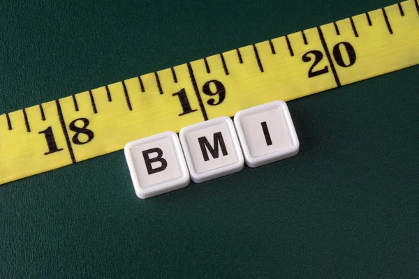 Arrangement of alphabet blocks of word BMI with yellow tape measure