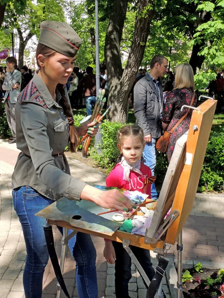 Drawing girl in field cap with easel in the park
