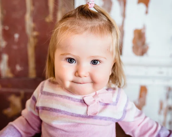 Close-up portrait of funny blond little girl with big grey eyes and plump cheeks with pursed lips. Studio portrait on grunge background