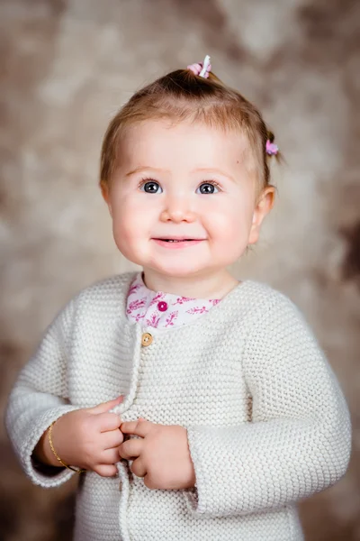 Portrait of smiling blond little girl with big grey eyes and plump cheeks. Studio portrait on brown grunge background