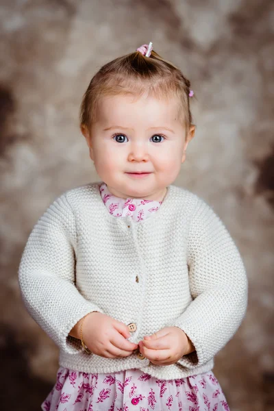 Portrait of beautiful blond little girl with big grey eyes and plump cheeks looking at camera. Studio portrait on brown grunge background