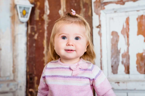 Surprised funny blond little girl with big grey eyes and plump cheeks looks up. Studio portrait on grunge wooden background