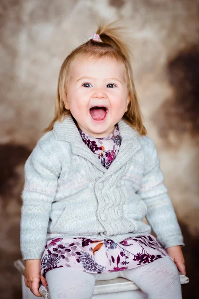 Cute little girl with blond hair sitting on white chair and laughing