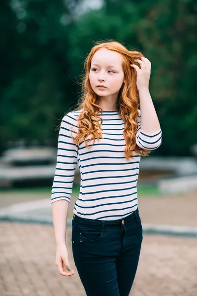 Outdoor portrait of beautiful girl with long curly red hair and green eyes. Young redhead woman touching her ginger hair. Teenage red-haired girl standing  in summer park. Femininity concept