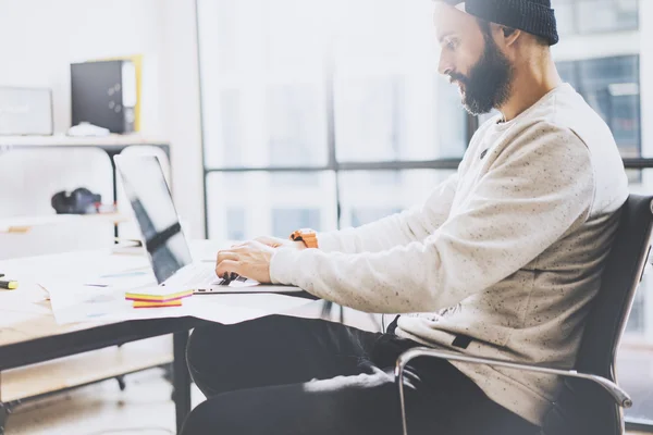 Bearded graphic designer working with new project modern loft. Generic design notebook on wood table.  Analyze plans, papers, hands keyboard. Blurred background, film effect