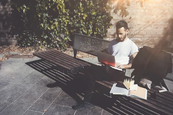 Photo man sitting city park bench and texting message notebook. Using wireless internet. Studying at the University,  preparation for exams. Use book, generic design laptop. Horizontal, soft shadows