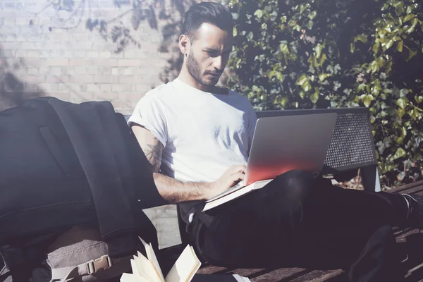 Photo student sitting city park bench and texting message notebook. Using wireless internet.Studying at the University,  preparation for exams.Use book, generic design laptop. Horizontal, soft shadows