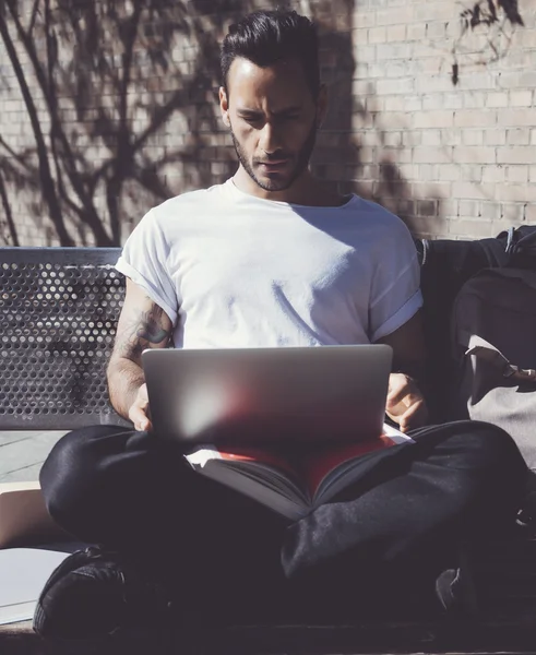 Photo man sitting city park bench and using laptop wireless internet. Studying at the University, working new project. Using book, generic design computer. Vertical