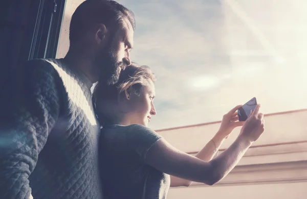Adult couple summer journey. Photo woman and bearded man making photo sunset mobile phone. Using contemporary smartphone, smiling. Horizontal, film effect.