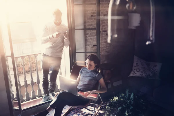 Couple professionals work together. Photo woman and bearded man working with new startup project in modern building. Using contemporary notebook, smartphone.Horizontal, film effect. Blurred background