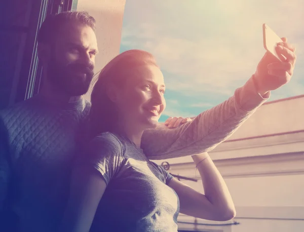 Young couple summer holiday city. Photo woman and bearded man making selfie mobile phone in modern loft. Using contemporary smartphone, smiling. Horizontal, sunlights effect.