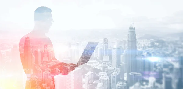 Double exposure photo bearded businessman wearing black shirt and glasses.Banker holding contemporary notebook hands,work online banking.Panoramic view modern skyscraper city background.Horizontal