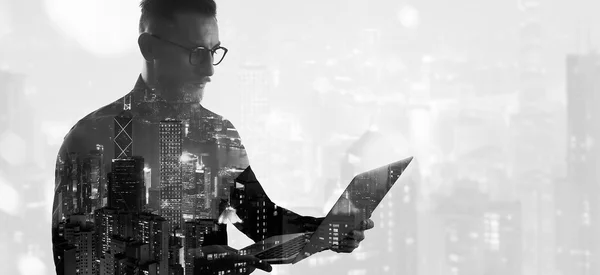 Double exposure bearded businessman wearing black shirt and glasses.Banker holding contemporary notebook hands,work online banking. Modern skyscraper city background. Wide mockup