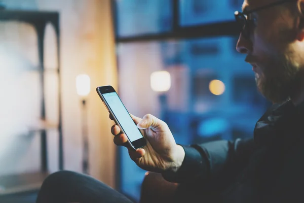 Closeup photo businessman relaxing modern loft office. Man sitting in chair at night. Using contemporary smartphone, blurred background. Horizontal, film, flares effect.