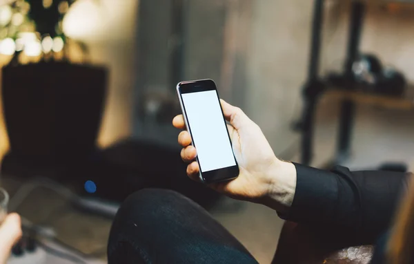 Photo man relaxing in modern loft studio.Man sitting chair night.Using contemporary smartphone,blurred background.Blank screen ready for your business information.Horizontal,film effect.