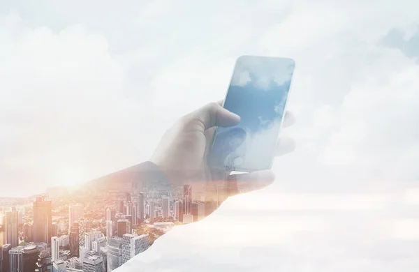 Double exposure photo businessman holding modern smartphone hand, touching empty screen. Reflection of clouds and contemporary city background. Horizontal mockup. Film effect