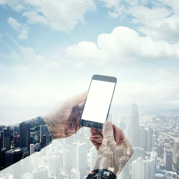 Double exposure photo businessman holding modern smartphone hands. Panoramic view contemporary city and clouds background. White blank screen ready for your business information. Square mockup.