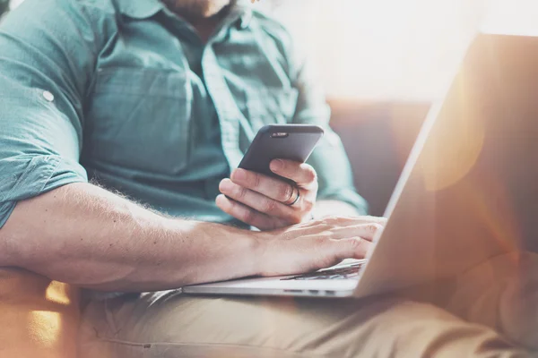 Bearded Businessman work Laptop modern Design Interior Loft Studio .Man relaxing Vintage Sofa.Use contemporary Notebook Send Message Smartphone.Blurred background.Creative Process Startup Idea.Film