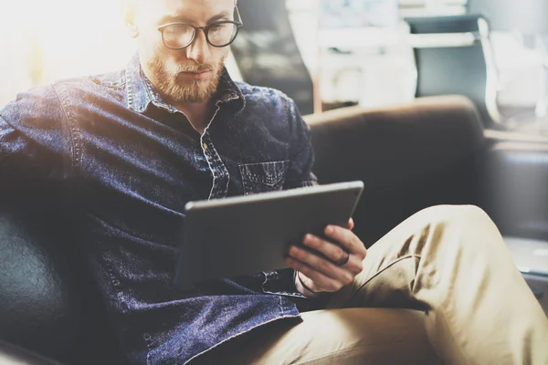 Bearded Hipster working tablet computer modern Interior Design Loft Office.Man relax Vintage sofa use contemporary device Hand.Blurred Background.Creative Business Startup Idea.Closeup.Film effect.