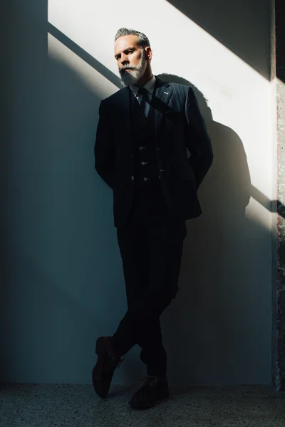 Stylish bearded man wearing trendy suit and stands against the wall. Vertical