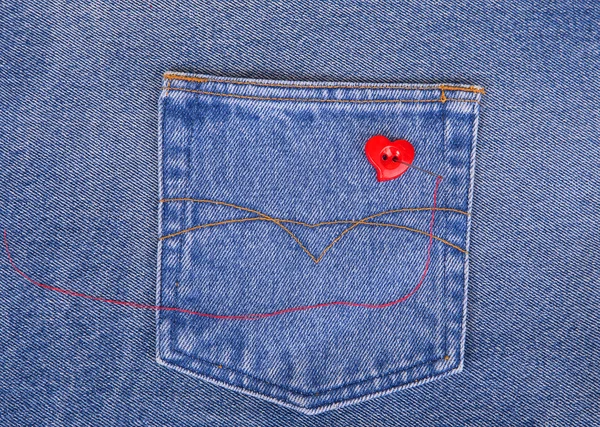 Red heart shaped button with needle and red thread on denim fabr