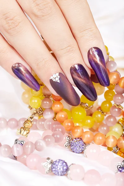 Hand with long artificial manicured nails holding a necklace