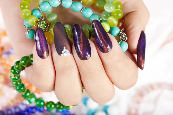 Hand with long artificial manicured nails holding colorful bracelets