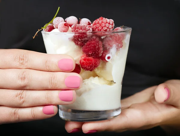 Hands with pink manicured nails holding a jar with ice cream and berries