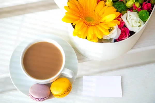 Cup of coffee with cookies on a wooden background is next to the box with flowers