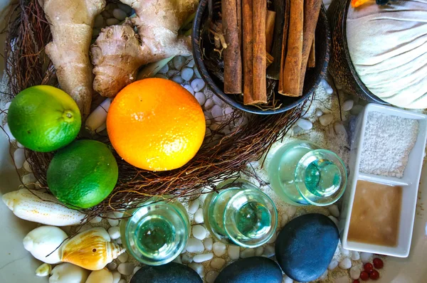 Top flat view of spa ingredients: oil in glass jars, orange, lyme, ginger, cinnamon sticks, stones, sand
