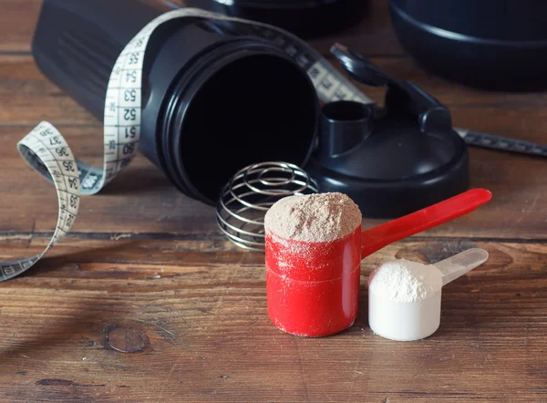 Whey protein powder in scoop with vitamins on plate on wooden background
