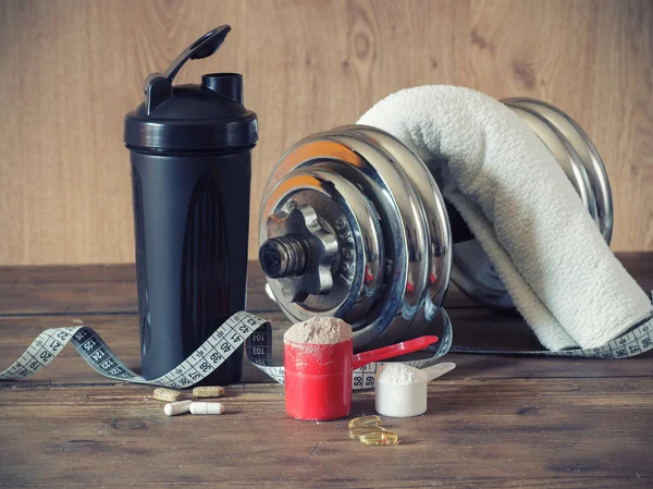 Whey protein powder in scoop with vitamins on plate on wooden background