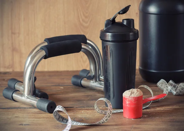 Whey protein powder in scoop and plastic shaker on wooden background