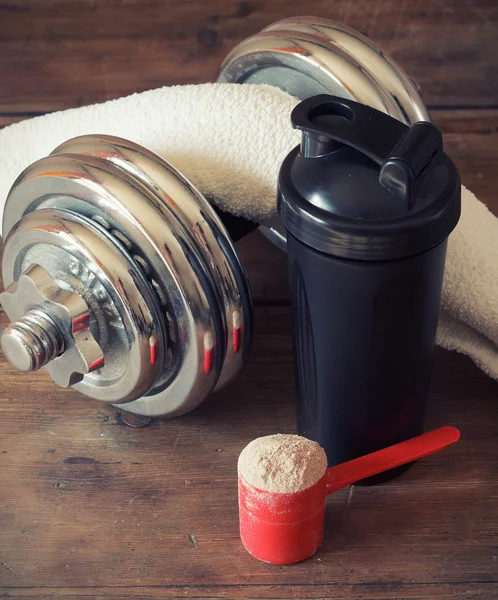 Whey protein powder in scoop and plastic shaker on wooden background