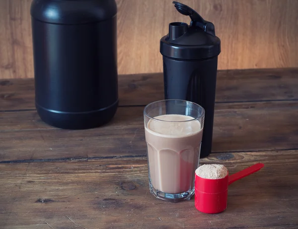 Whey protein powder in scoop and plastic shaker on wooden background