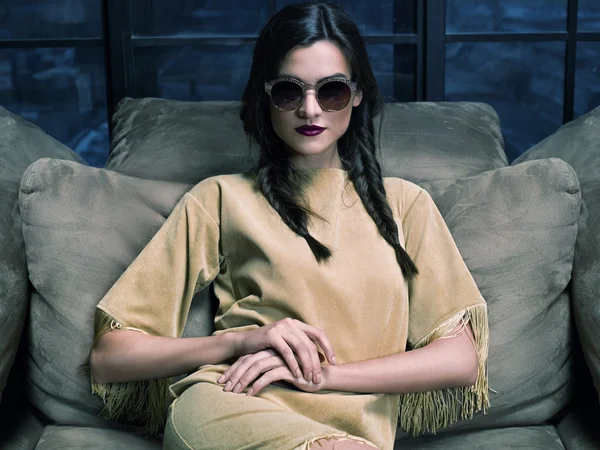 Elegant fashion model wearing mustard dress, sitting on the couch