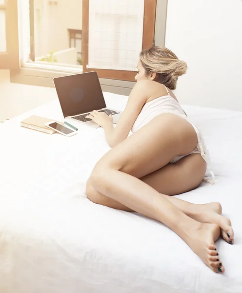 Young sensual latin woman relaxing in bed with laptop