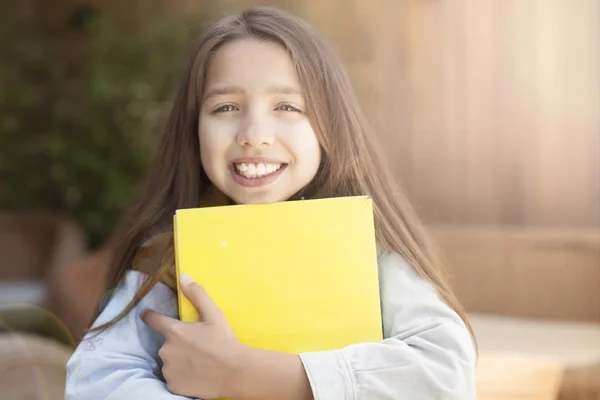 Smiling little student girl with many books at school