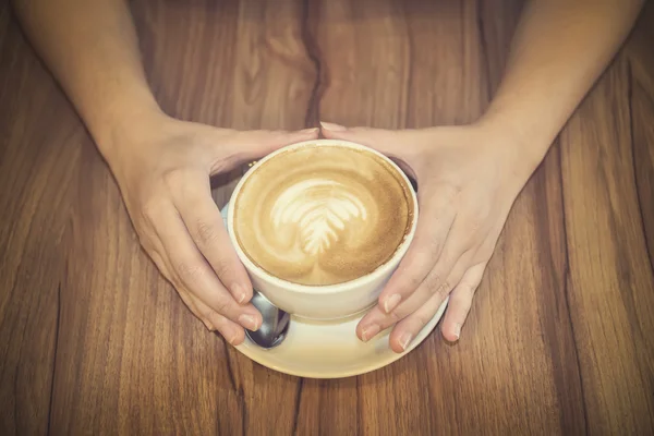 Hand holding coffee cup on wood table.